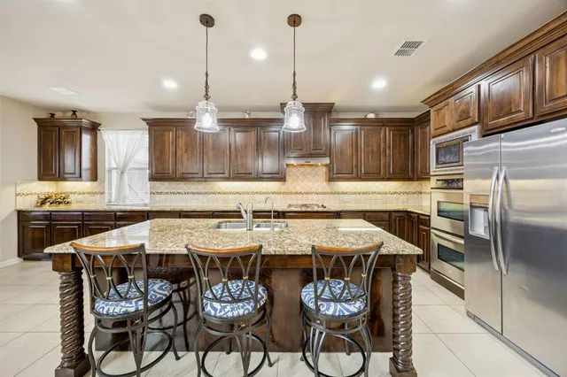 a kitchen with stainless steel appliances granite countertop a sink a stove a refrigerator and chairs