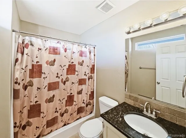 a bathroom with a granite countertop sink toilet a mirror and shower curtain