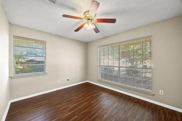 an empty room with wooden floor fan and windows