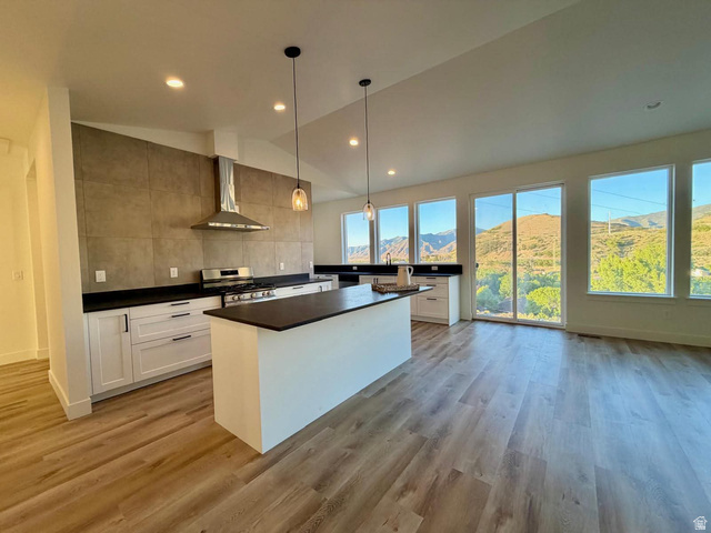 905 Settlement Canyon Road Tooele, UT 84074 - Photo 5 of 12 Open-concept kitchen featuring white cabinetry, dark countertops, a stainless steel range with a professional-grade hood, a central island, and wood-finish flooring, complemented by multiple large windows overlooking a mountainous landscape
