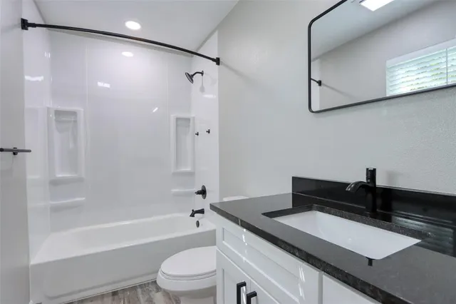 a bathroom with a granite countertop sink a toilet a mirror and bathtub