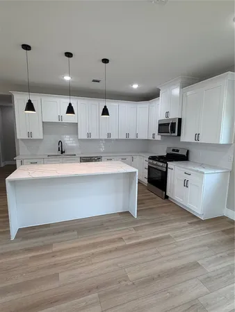 a large kitchen with stainless steel appliances granite countertop a stove a sink dishwasher a microwave oven and a white countertops with wooden floor