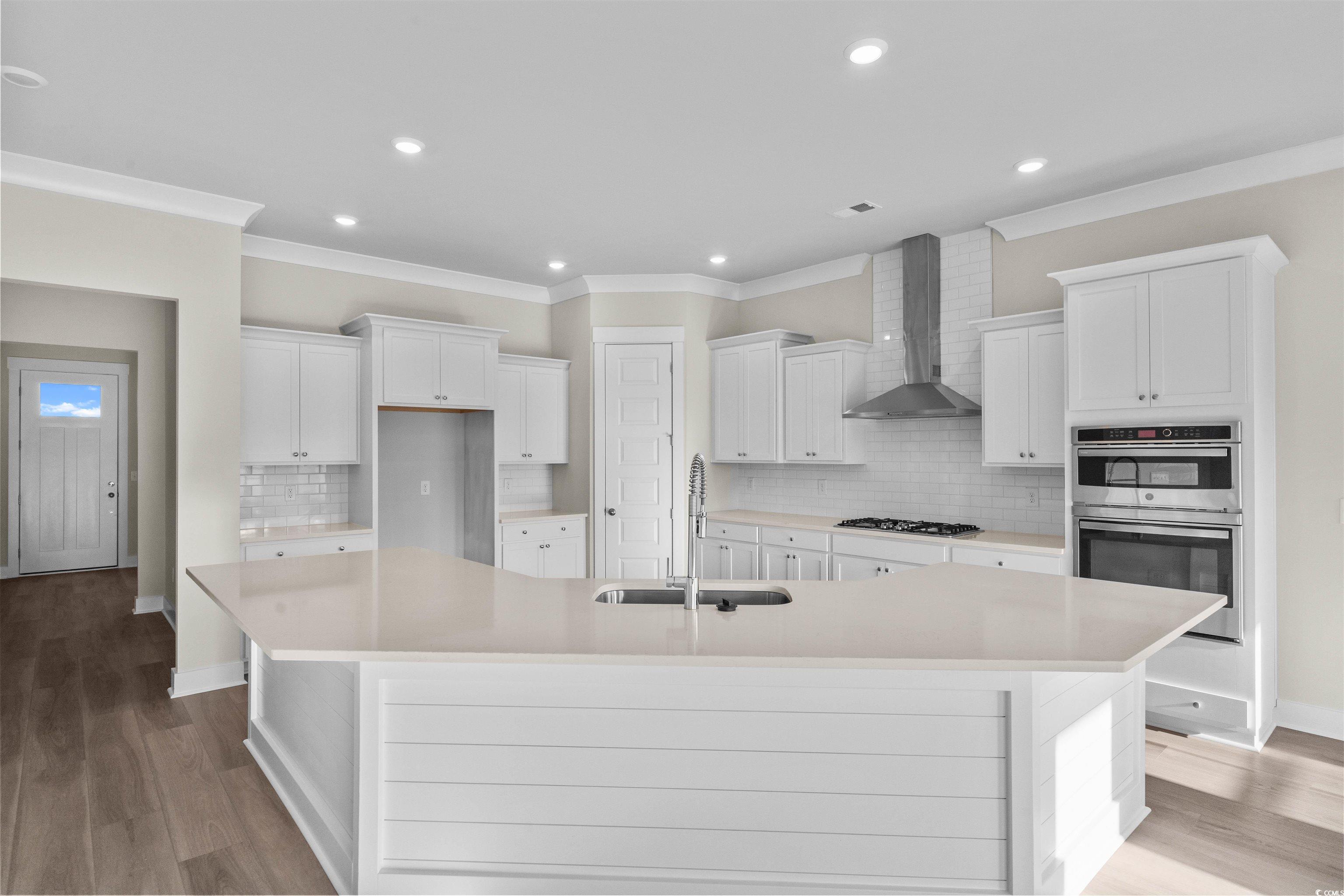 205 Atlantic Breeze Street Myrtle Beach, SC 29572 - Photo 5 of 28 Kitchen featuring white cabinets, ornamental molding, a large island with sink, wall chimney exhaust hood, and decorative backsplash