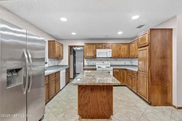 a large kitchen with stainless steel appliances kitchen island granite countertop a refrigerator a sink a stove and island