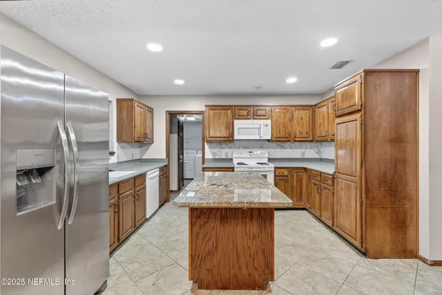 a large kitchen with stainless steel appliances kitchen island granite countertop a refrigerator a sink a stove and island