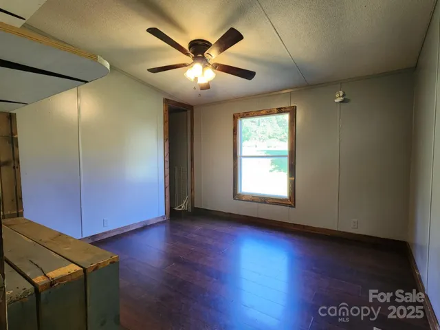 an empty room with wooden floor chandelier fan and windows