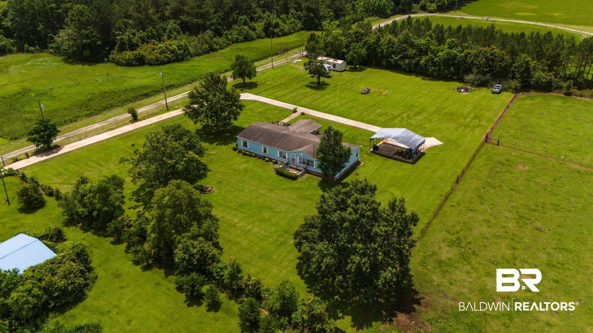 34985b Spring Road South, Unit B Stapleton, AL 36578 - Photo 29 of 31 Expansive green acreage featuring a single-story residence with a light blue exterior, a detached covered structure, a long driveway, and mature trees