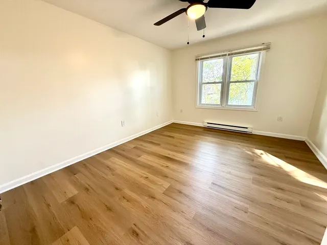 an empty room with wooden floor chandelier fan and windows