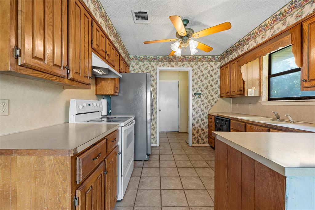 116 Boleman Drive Hewitt, TX 76643 - Photo 11 of 38 Kitchen with white electric range, brown cabinetry, under cabinet range hood, light countertops, and a textured ceiling
