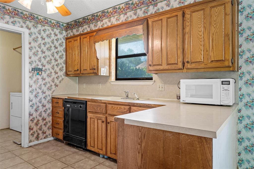 116 Boleman Drive Hewitt, TX 76643 - Photo 12 of 38 Kitchen featuring wallpapered walls, brown cabinets, light countertops, white microwave, and a textured ceiling