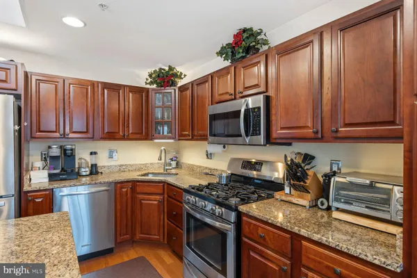 a kitchen with stainless steel appliances granite countertop a stove a sink dishwasher and a microwave oven with wooden cabinets