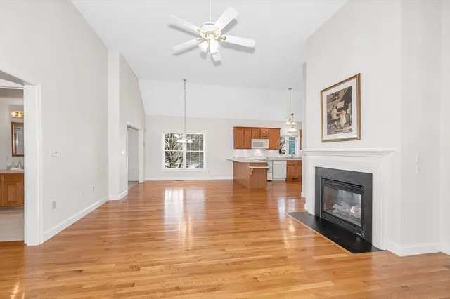 a view of a livingroom with a fireplace a ceiling fan and kitchen view