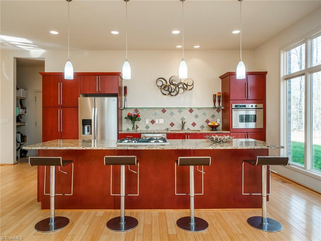 725 Hudson Road Summerfield, NC 27358 - Photo 5 of 36 Custom cabinet kitchen with all stainless steel appliances large island with seating, glass backsplash and views of the backyard.