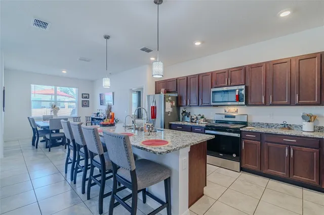 a kitchen with stainless steel appliances granite countertop a stove top oven a refrigerator a sink dishwasher a dining table and chairs with wooden floor
