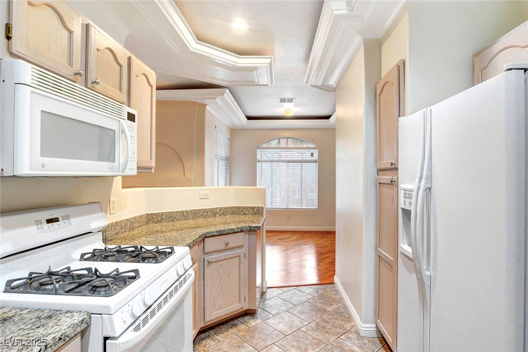 8725 Red Rio Drive, Unit 203 Las Vegas, NV 89128 - Photo 12 of 38 Kitchen featuring white appliances, crown molding, baseboards, light brown cabinets, and light stone counters