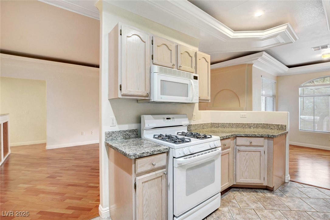 8725 Red Rio Drive, Unit 203 Las Vegas, NV 89128 - Photo 10 of 38 Kitchen featuring white appliances, crown molding, light wood-style flooring, a tray ceiling, and a peninsula