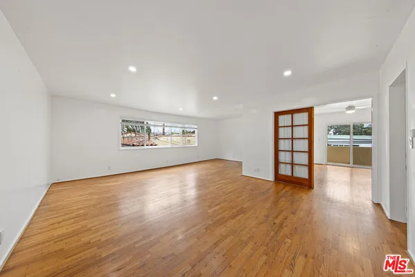 an empty room with wooden floor kitchen view and windows