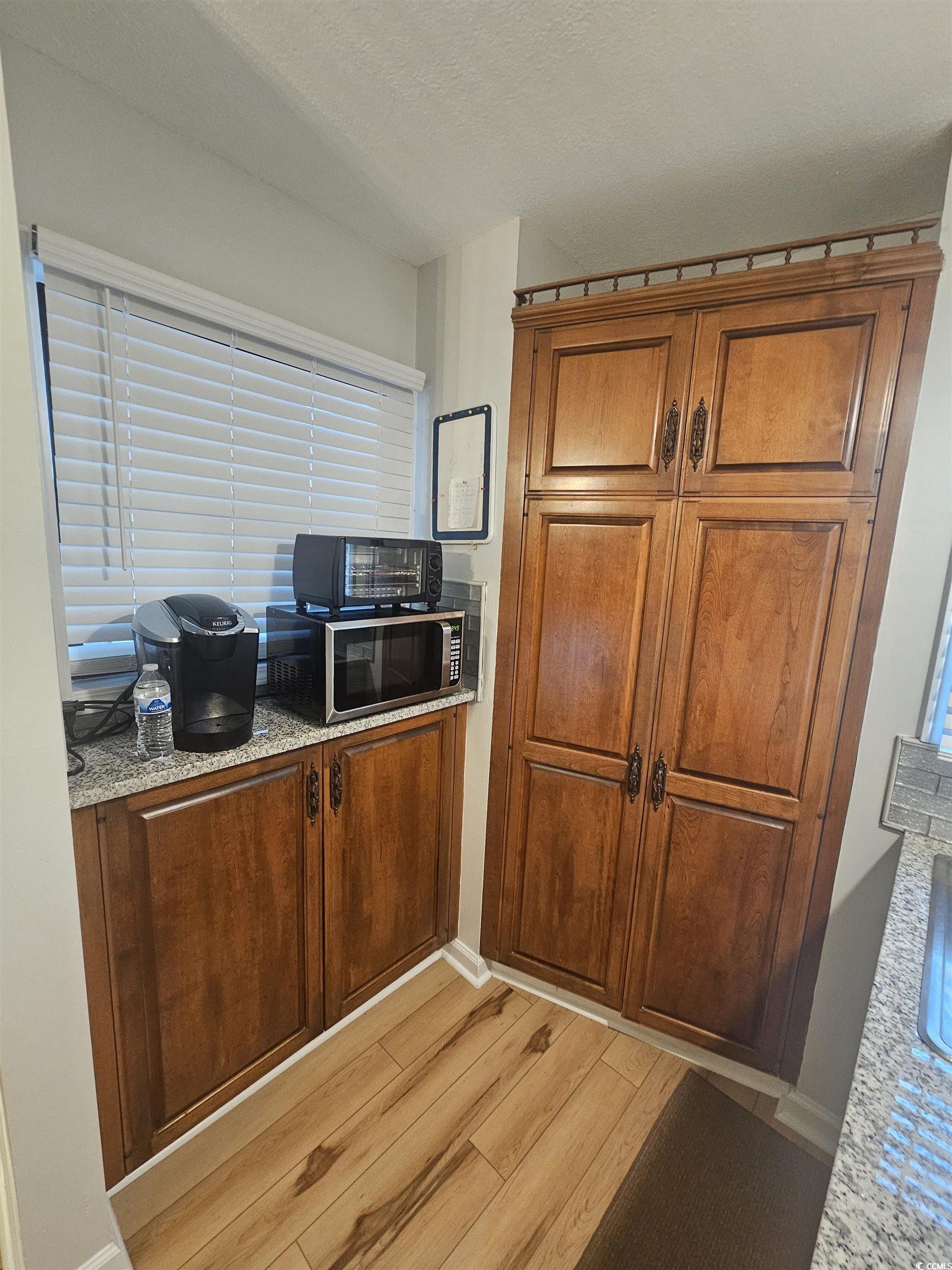 1910 South Ocean Boulevard, Unit C2 NASSAU I North Myrtle Beach, SC 29582 - Photo 8 of 12 Kitchen with brown cabinetry, light wood-style flooring, a textured ceiling, stainless steel microwave, and light stone counters