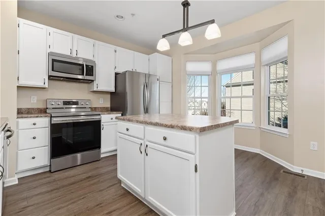 a kitchen with stainless steel appliances granite countertop a stove a sink dishwasher a refrigerator white cabinets and wooden floor