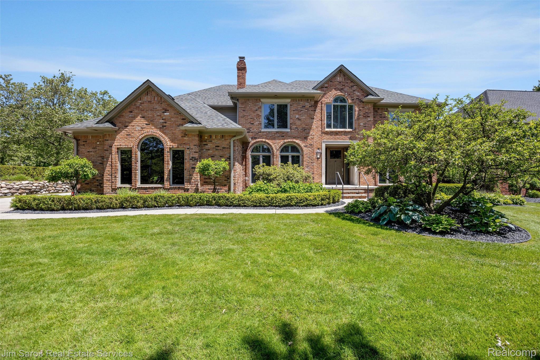 Brick facade residence featuring multiple arched windows, prominent gables, and a mature landscaped front yard
