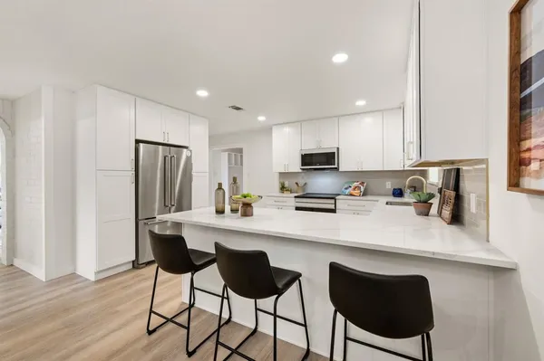 a kitchen with stainless steel appliances a dining table chairs refrigerator and sink