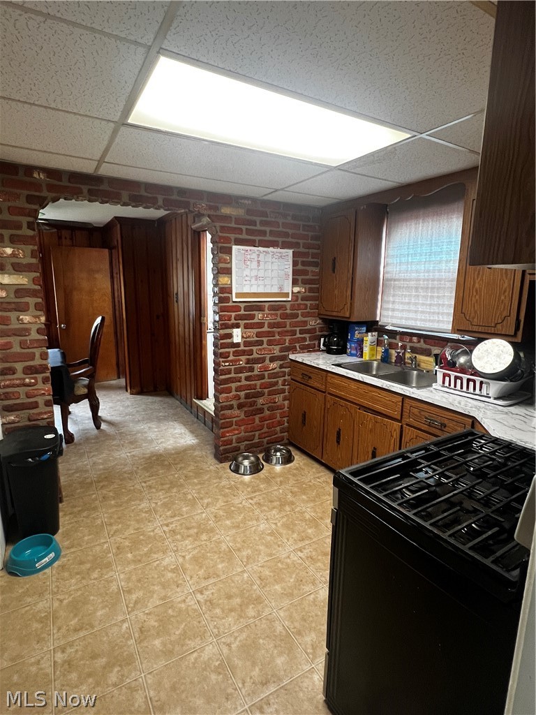 19529 Libby Road Maple Heights, OH 44137 - Photo 5 of 13 Kitchen featuring a drop ceiling, light tile flooring, brick wall, range, and sink