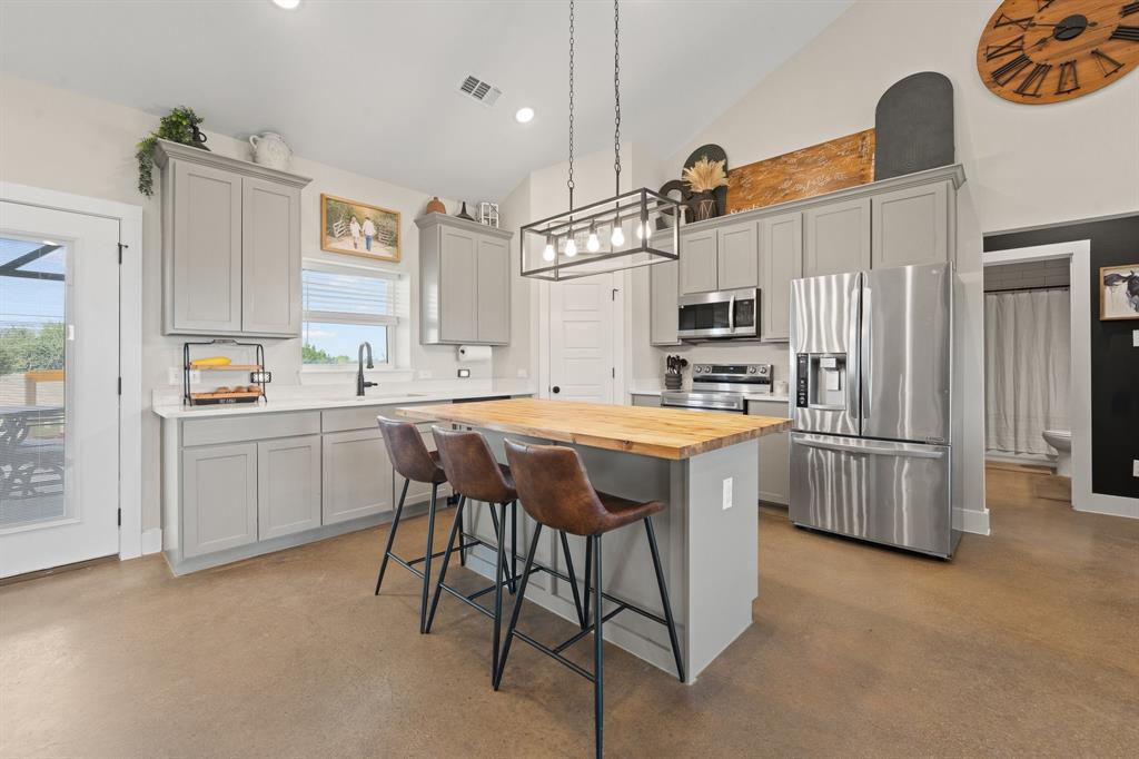 1031 Augustus Court Rio Vista, TX 76093 - Photo 5 of 30 Open-concept kitchen featuring an island with a wood-finish countertop, light gray cabinetry, stainless steel appliances, and concrete flooring