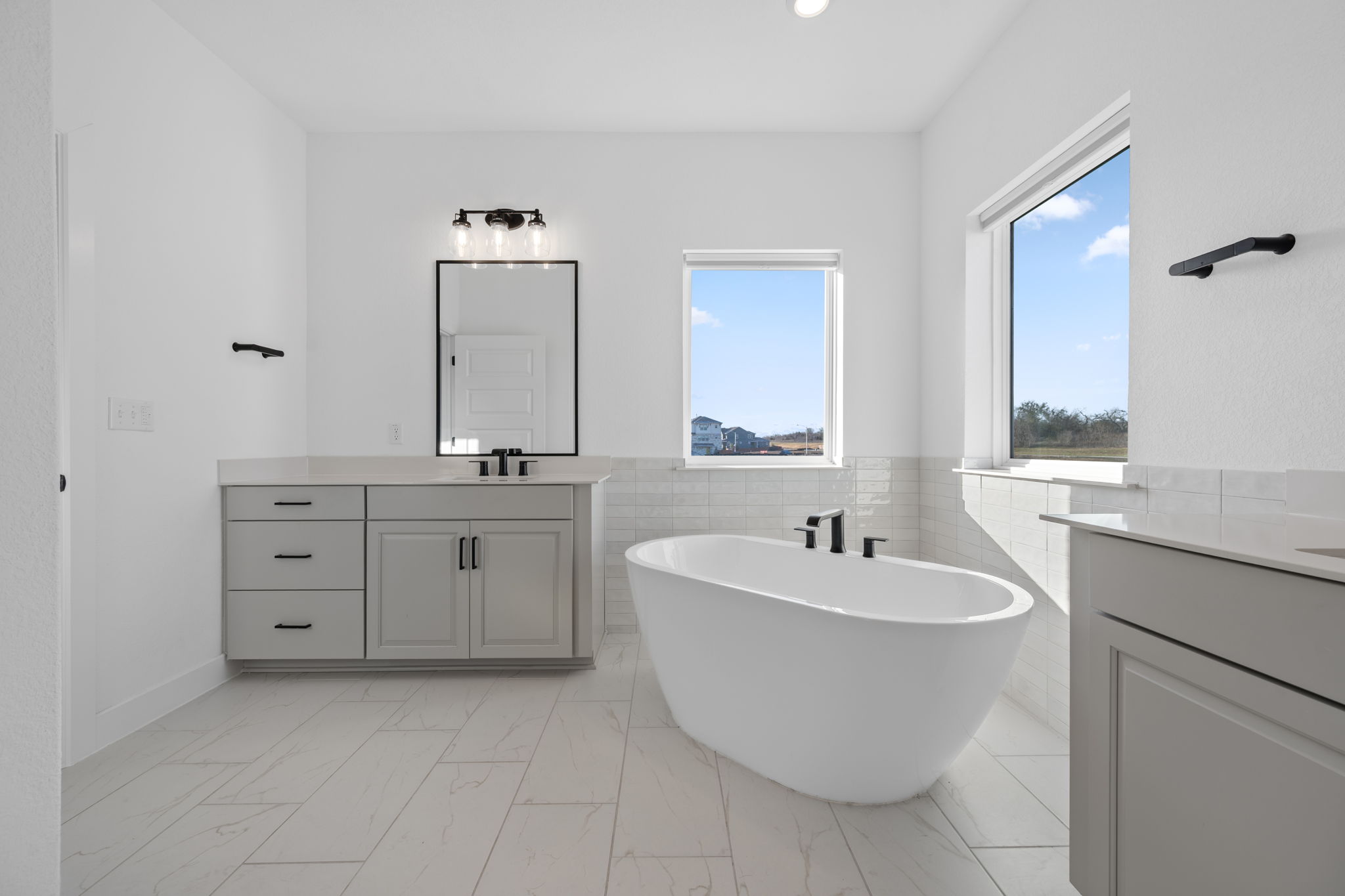 5902 Rangeland Road Austin, TX 78747 - Photo 22 of 35 Full bathroom with tile walls, a freestanding bath, two vanities, a wainscoted wall, and light marble finish floors