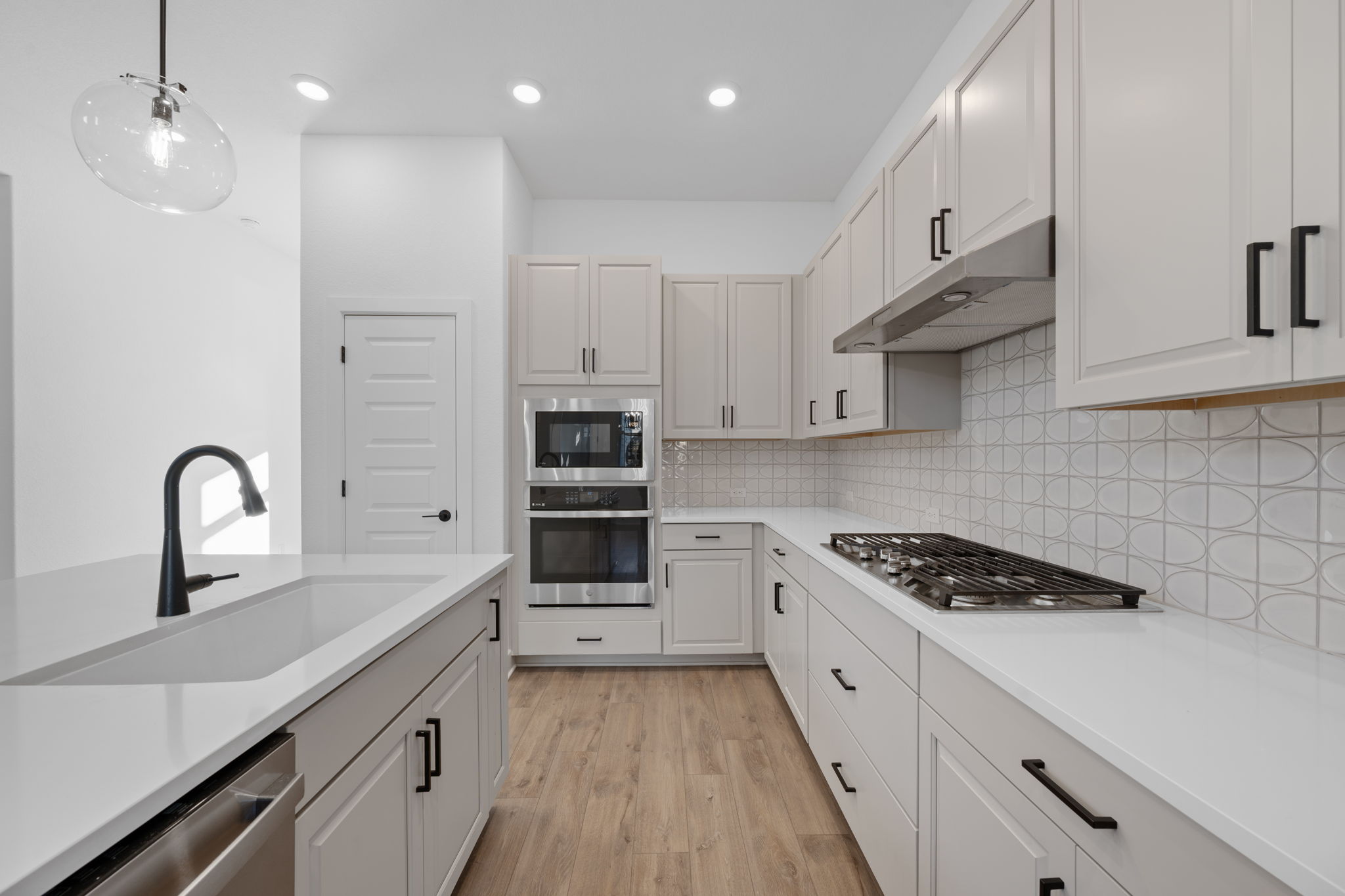 5902 Rangeland Road Austin, TX 78747 - Photo 10 of 35 Kitchen with light wood-style flooring, appliances with stainless steel finishes, decorative light fixtures, under cabinet range hood, and light stone countertops