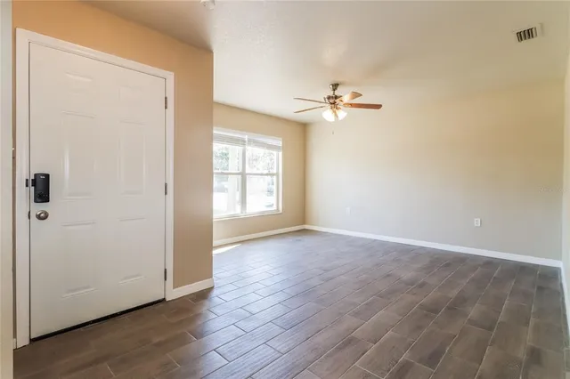 an empty room with wooden floor ceiling fan and window
