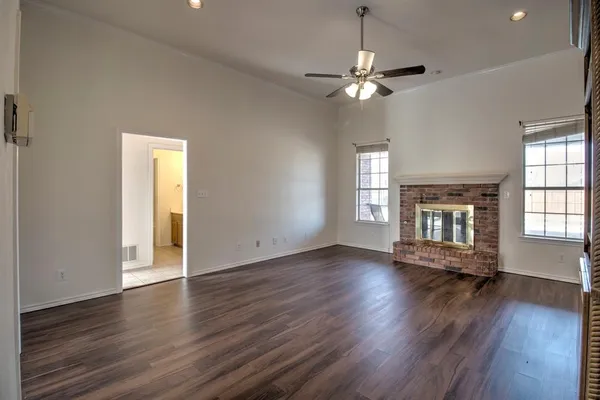 a view of an empty room with wooden floor fireplace and a window