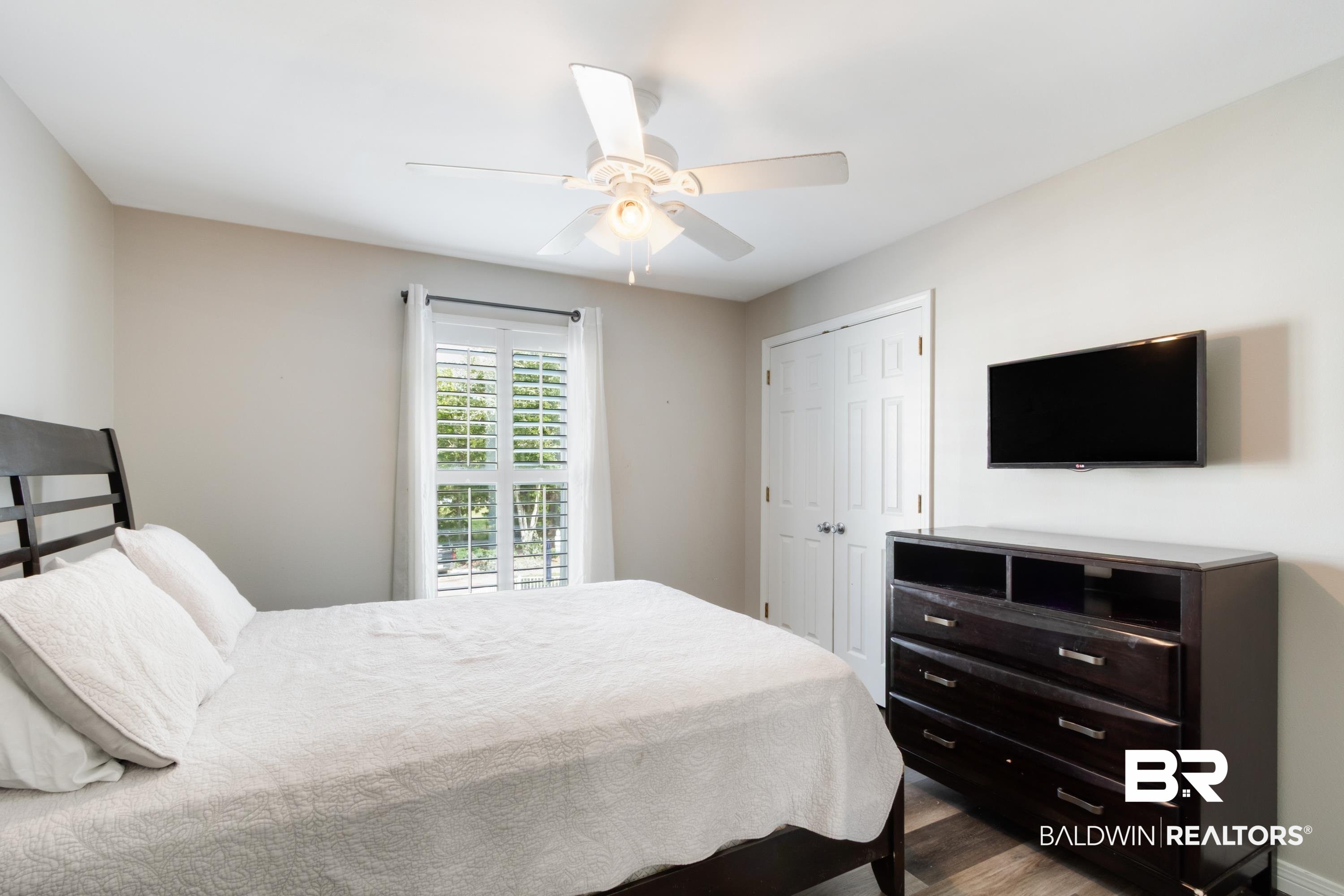 25957 Canal Road, Unit 208 Orange Beach, AL 36561 - Photo 18 of 28 Bedroom featuring a window with plantation shutters, a ceiling fan, wood-finish flooring, and a bifold door closet