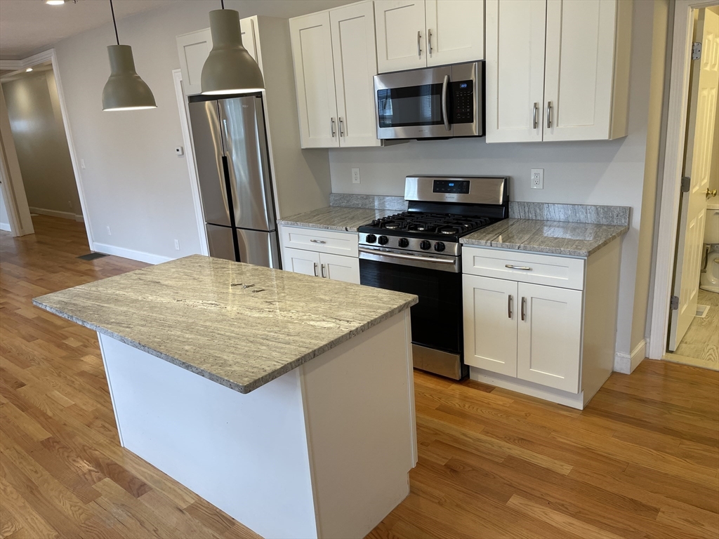 a kitchen with stainless steel appliances a stove a refrigerator a sink a stove and white cabinets with wooden floor