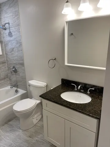 a bathroom with a granite countertop sink toilet mirror and bathtub
