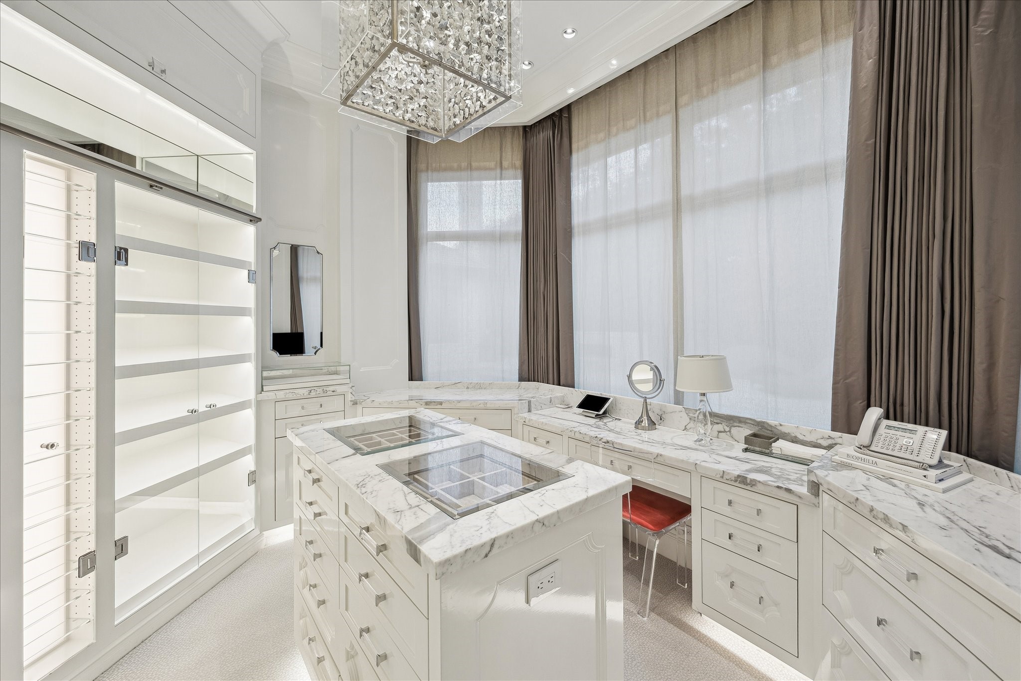 220 Merrie Way Lane Houston, TX 77024 - Photo 25 of 50 Luxury meets function in this designer primary closet, including a built-in vanity, soft-close drawers, backlit sunglasses and display cases, bench seating, and a statement butterfly chandelier.
