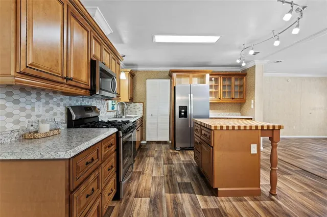 a kitchen with stainless steel appliances granite countertop a refrigerator a sink dishwasher a stove and a dining table with wooden floor