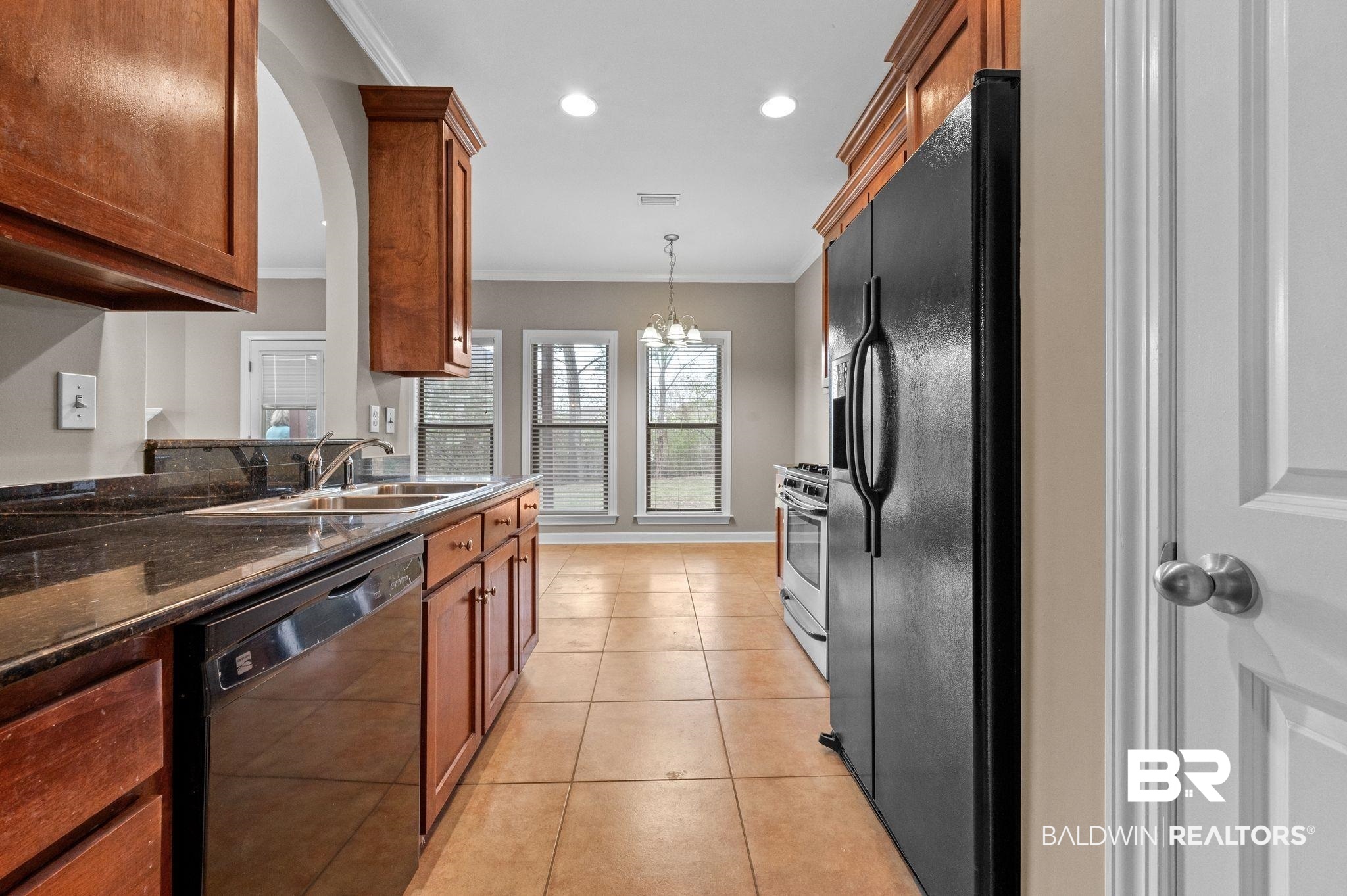 9381 Sable Court Daphne, AL 36526 - Photo 14 of 42 Kitchen with light tile patterned floors, dark stone counters, brown cabinets, crown molding, and black appliances