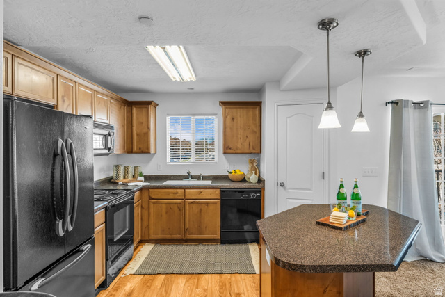 1136 West Spencer Road, Unit Y203 Pleasant Grove, UT 84062 - Photo 8 of 26 Kitchen with black appliances, dark countertops, a center island, wood finish cabinets, and light wood-style floors