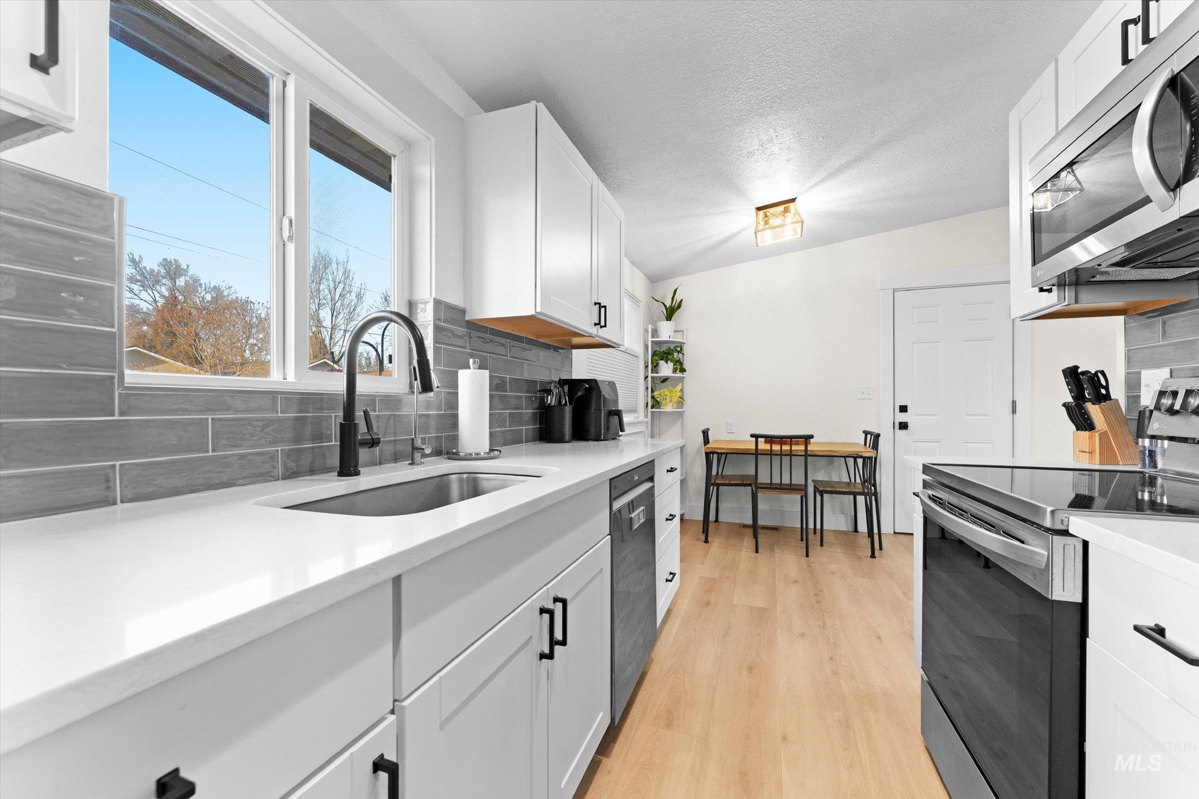 406 Chestnut Street Mountain Home, ID 83647 - Photo 7 of 31 Kitchen with stainless steel appliances, white cabinets, light wood-style floors, a textured ceiling, and light stone counters