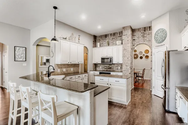 a kitchen with stainless steel appliances granite countertop a refrigerator a stove a sink dishwasher and white cabinets with wooden floor