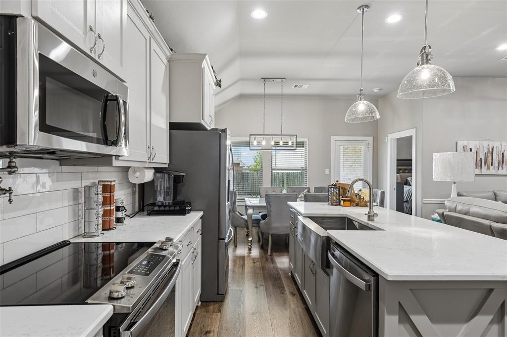 108 Maverick Lane Pilot Point, TX 76258 - Photo 12 of 27 Modern kitchen featuring stainless steel appliances, white subway tile backsplash, white shaker cabinetry, an expansive island with a farmhouse sink, and wood-finish flooring