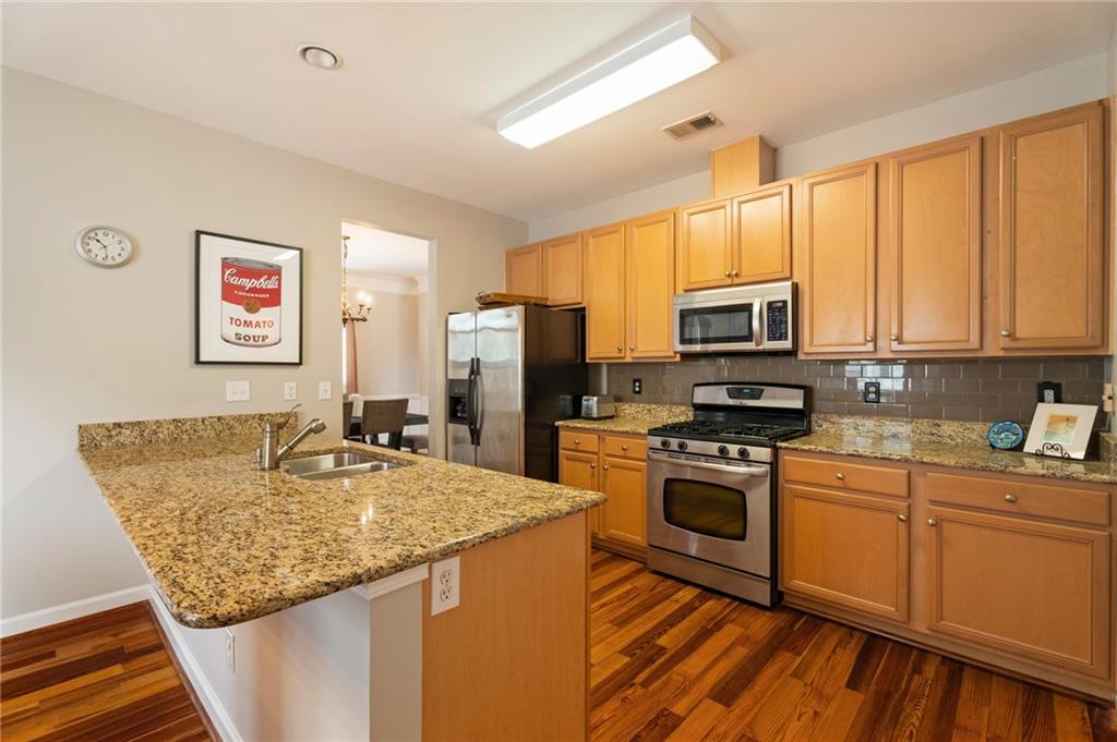 878 Scales Road Suwanee, GA 30024 - Photo 7 of 17 a kitchen with stainless steel appliances granite countertop a stove top oven a sink dishwasher and a refrigerator with wooden floor