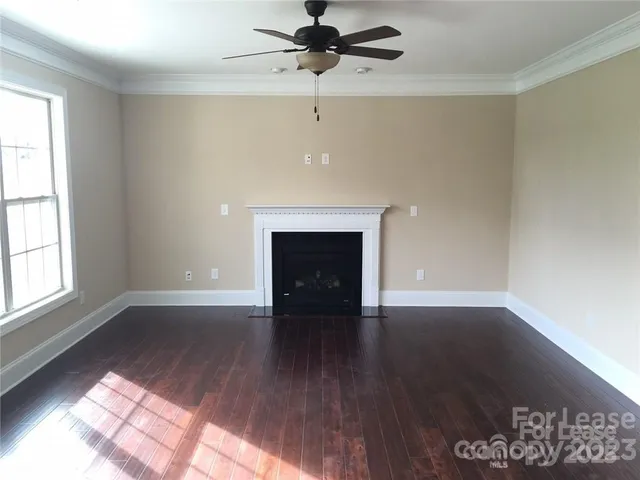 a view of an empty room with wooden floor fireplace and a window