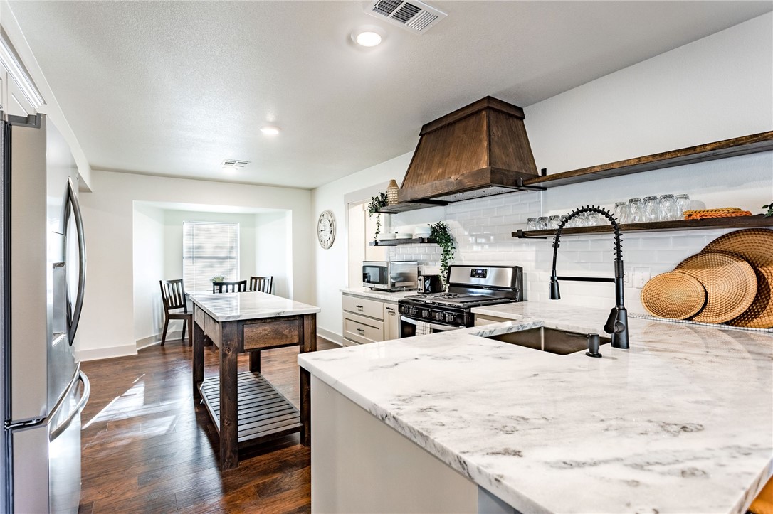 107 Spring Creek Street Waco, TX 76705 - Photo 20 of 78 a kitchen with stainless steel appliances kitchen island granite countertop a stove a refrigerator and a dining table with wooden floor