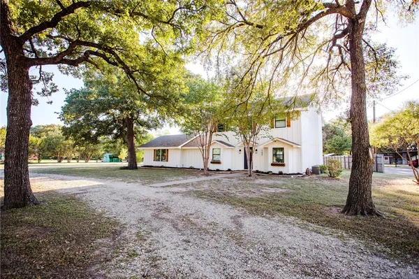 a view of white house with a big yard and large tree