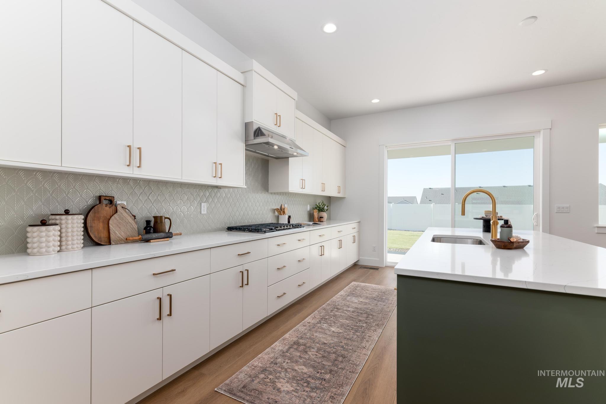 14703 Serenity Pt Street Caldwell, ID 83607 - Photo 12 of 45 Modern kitchen featuring extensive white cabinetry, a green kitchen island with an integrated sink and gold-finish faucet, white countertops, and a patterned tile backsplash