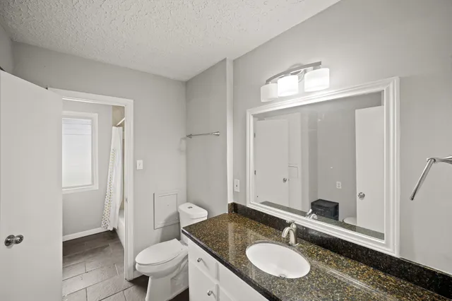 a bathroom with a granite countertop sink a toilet a mirror and a shower