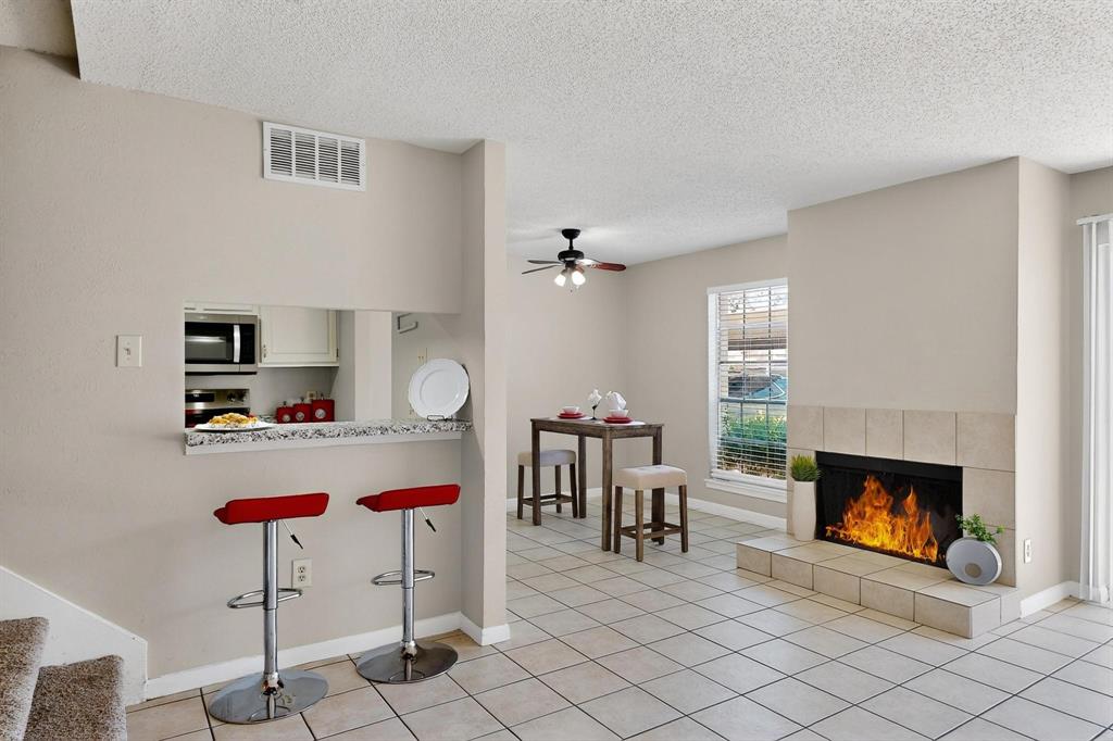 11311 Audelia Road, Unit 165 Dallas, TX 75243 - Photo 15 of 31 Kitchen featuring appliances with stainless steel finishes, a kitchen bar, a tiled fireplace, a ceiling fan, and a textured ceiling