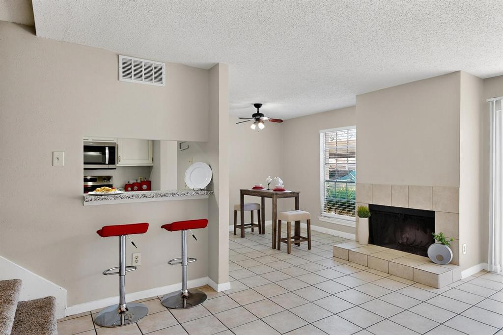 11311 Audelia Road, Unit 165 Dallas, TX 75243 - Photo 7 of 31 Kitchen with stainless steel microwave, a kitchen breakfast bar, a ceiling fan, light tile patterned flooring, and a textured ceiling