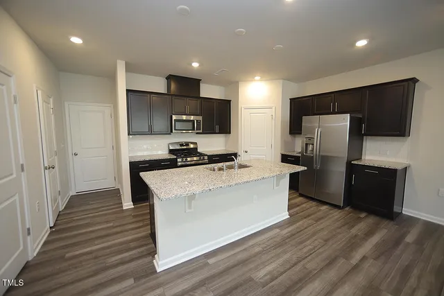 a large kitchen with stainless steel appliances wooden floor and a refrigerator